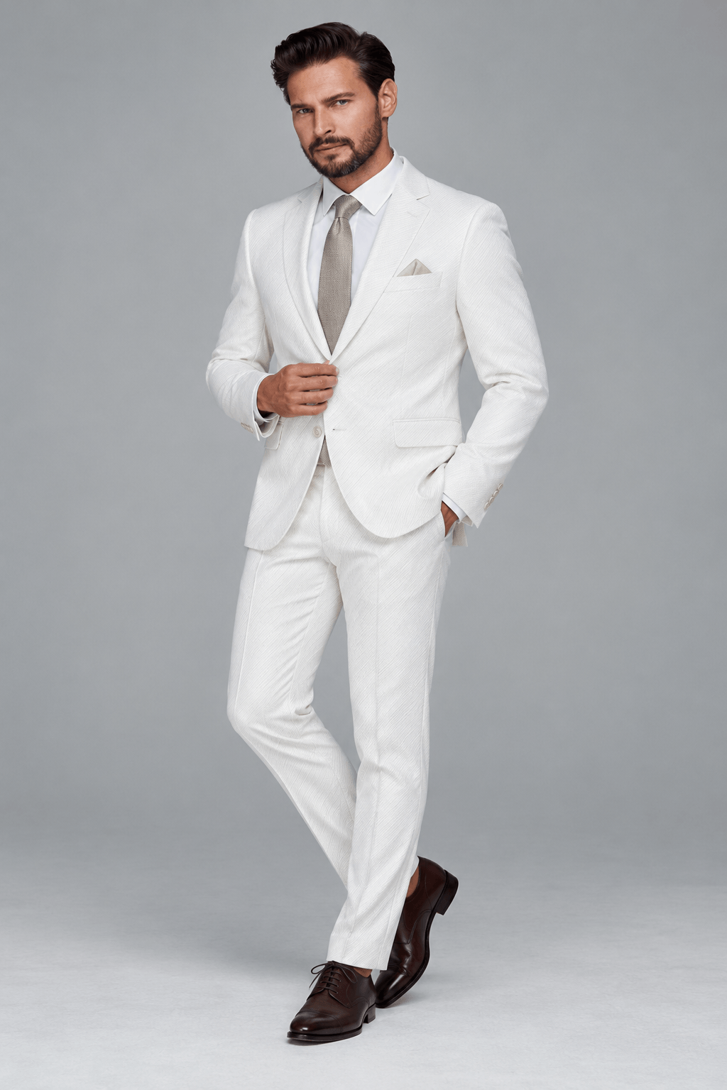 Man wearing a tailored ivory white textured two-piece suit with a white dress shirt, champagne-colored tie, matching pocket square, and dark brown leather Oxford shoes.