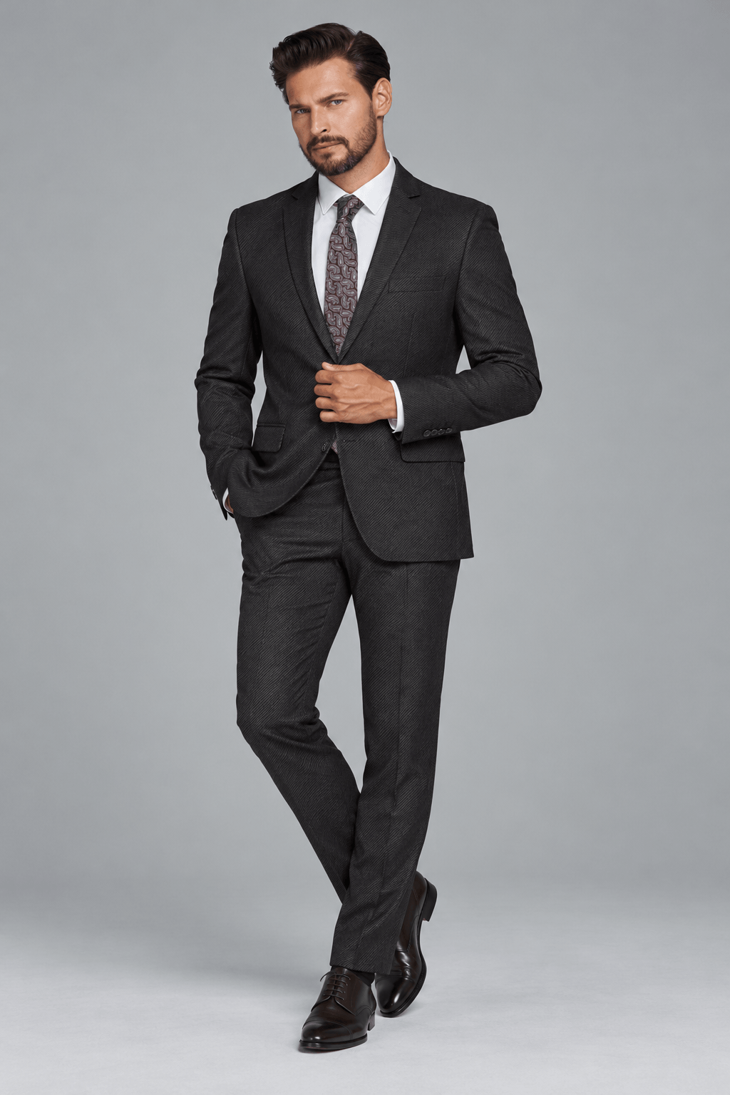Man wearing a tailored charcoal black textured two-piece suit with a white dress shirt, paisley-patterned tie, and dark brown leather Oxford shoes for a sophisticated formal look.