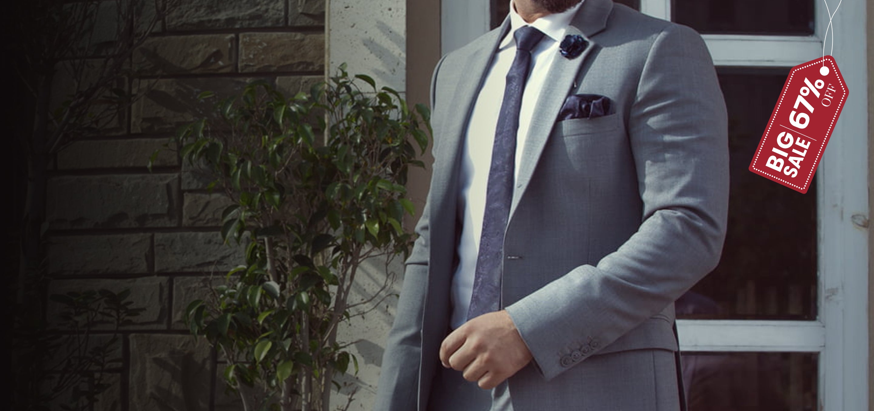 Man in a gray suit standing in front of a stone wall with a red sale tag.