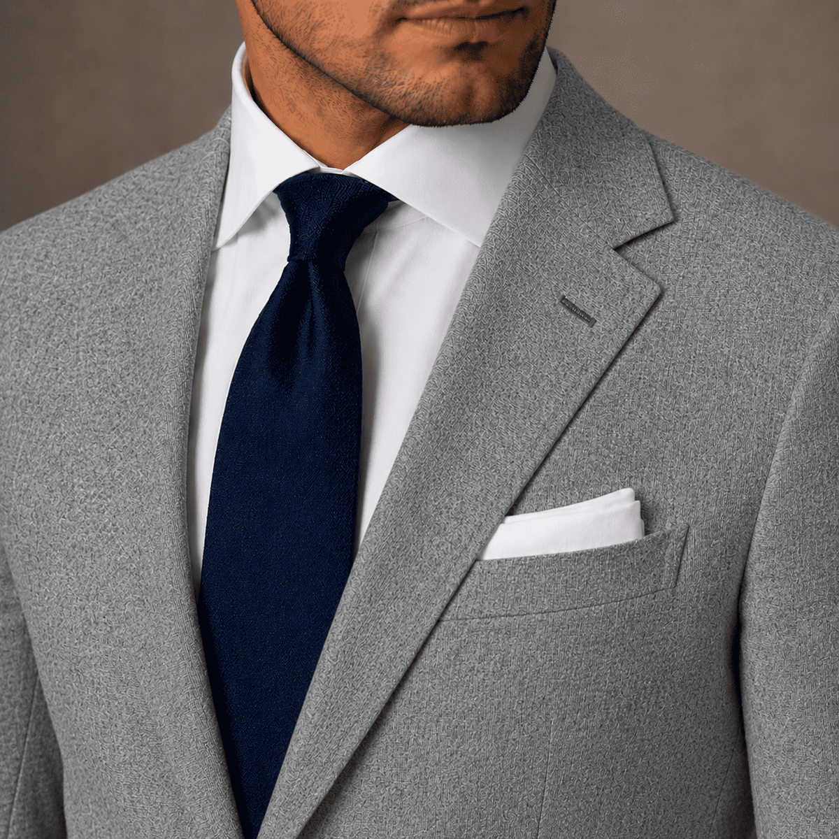Close-up of a men’s grey linen bespoke suit with textured fabric, white dress shirt, navy tie and white pocket square.