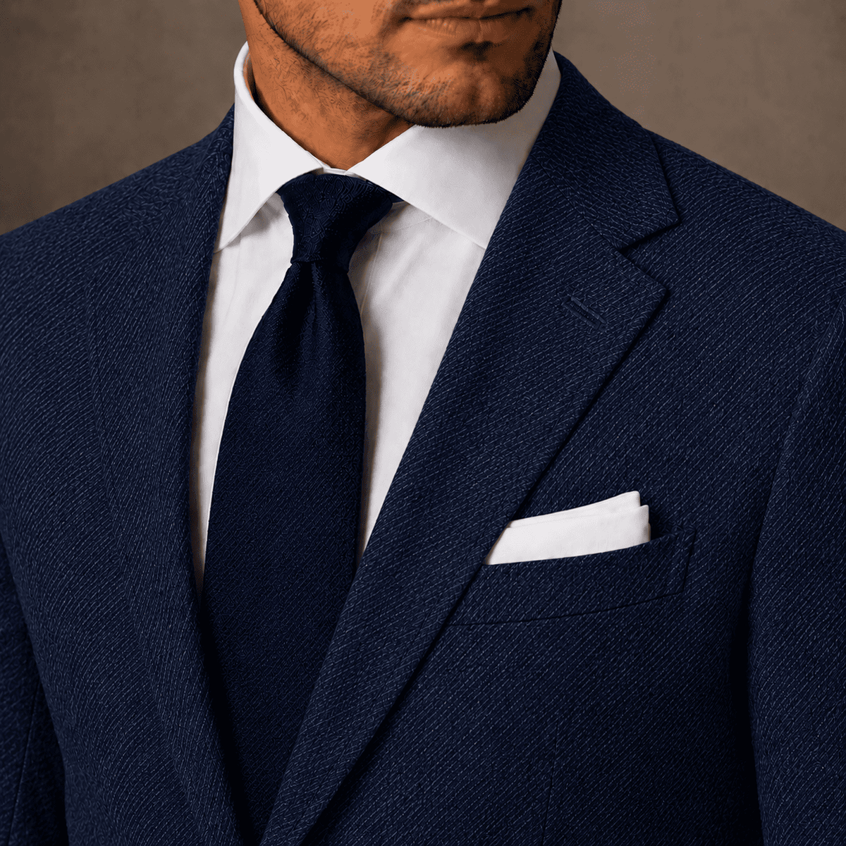 Close-up of a navy linen bespoke suit showing the textured jacket lapel, white dress shirt, navy tie and white pocket square.