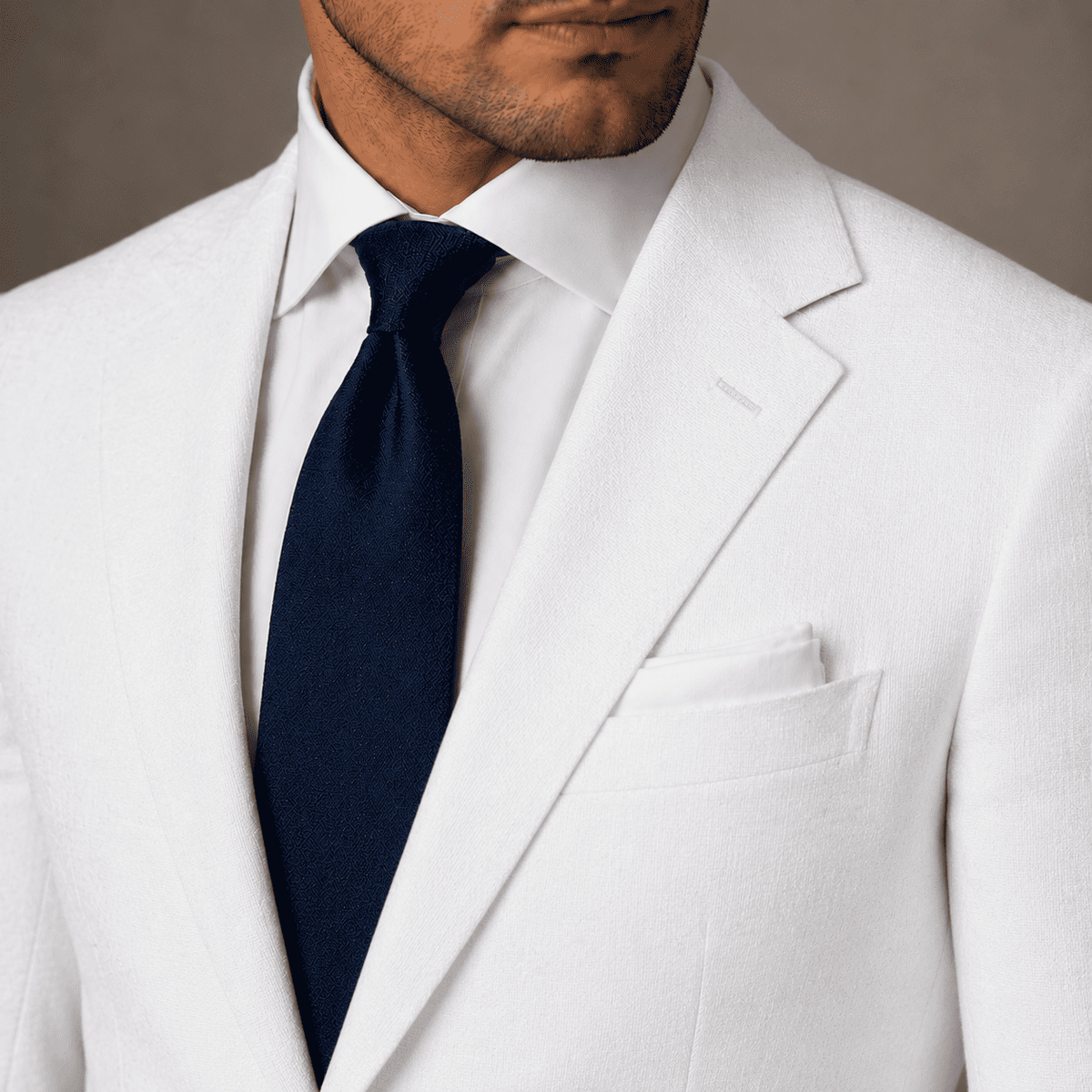 White linen bespoke suit jacket with a crisp white dress shirt, navy tie and white pocket square, highlighting the lightweight fabric and tailored lapel.